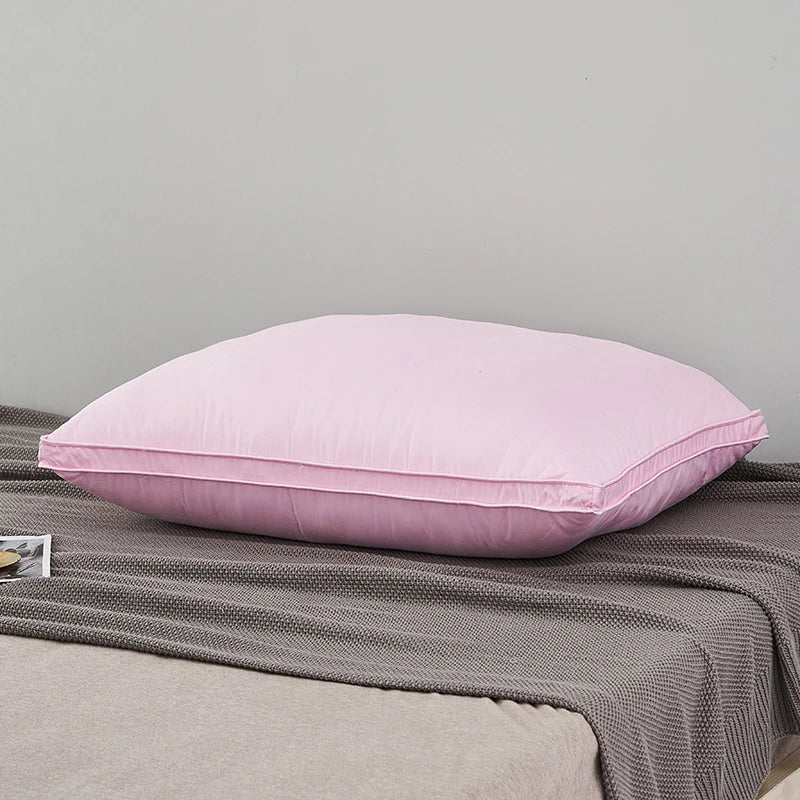 A pink luxury goose down and feather bed pillow resting on a gray blanket.