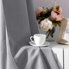 A white cup rests on a table next to a vase of pink and white flowers, with a gray curtain draped in the background.