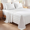 White satin bedding set with striped duvet and pillows on a wooden bed.