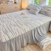A plush light blue linen bed skirt with vertical pleats covers a bed, next to a wooden dresser.