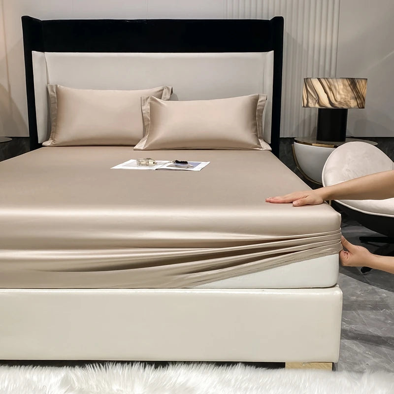A luxury bed featuring a fitted sheet and pillow set with beige bedding, white headboard, and modern bedside lamp.