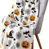 A white flannel blanket featuring a Halloween theme with black bats, spiders, and pumpkins draped over a gray chair.
