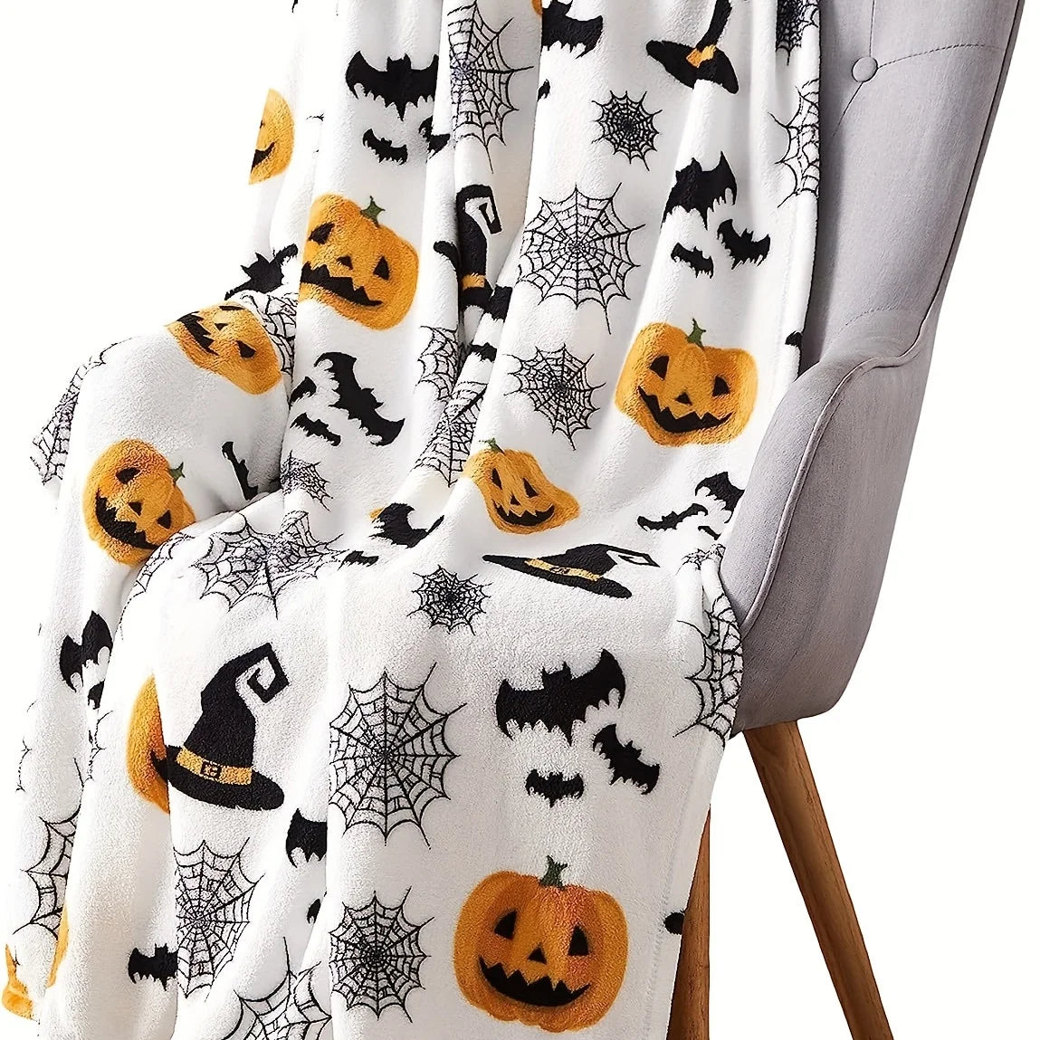 A white flannel blanket featuring a Halloween theme with black bats, spiders, and pumpkins draped over a gray chair.