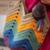A close-up of a handmade felted yarn object featuring multicolored geometric patterns in shades of yellow, green, blue, and p