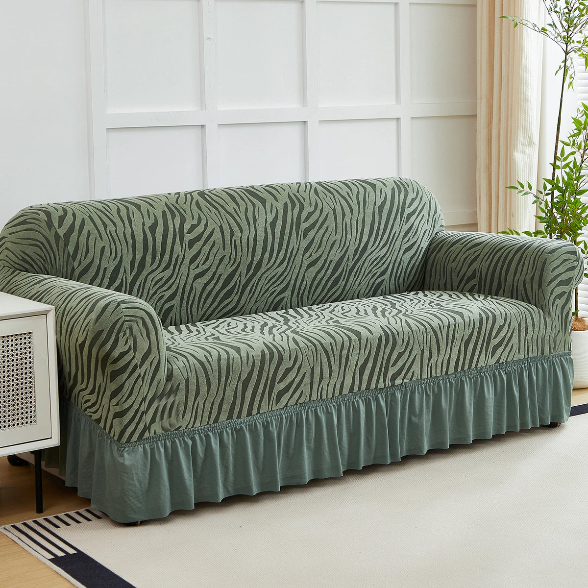 A teal anti-slip jacquard sofa slipcover draped on a light rug in a bright room.
