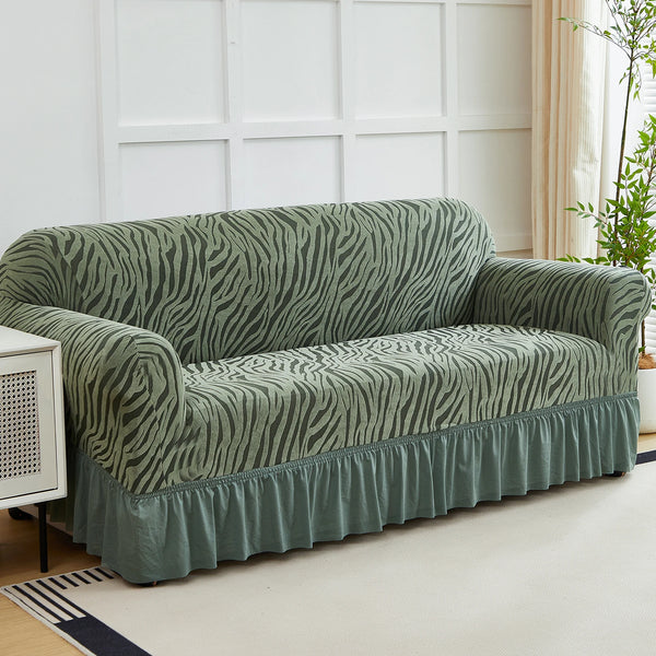 A teal anti-slip jacquard sofa slipcover draped on a light rug in a bright room.