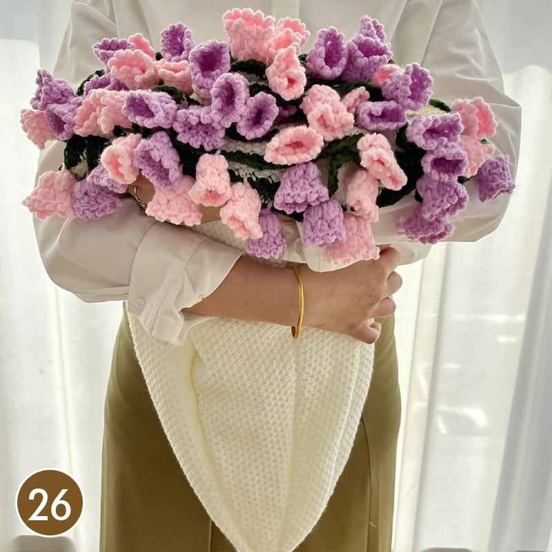 A hand knitted floral rose bouquet arrangement with pink and purple flowers held by a person wearing a white shirt and a crea