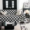 A black and white checkerboard sofa slipcover displayed on a dark table with decorative plants.