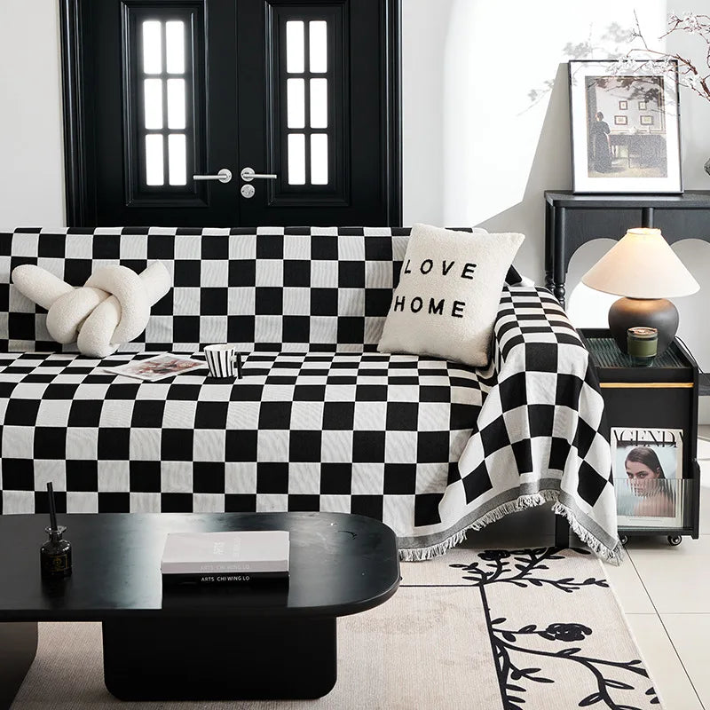 A black and white checkerboard sofa slipcover displayed on a dark table with decorative plants.