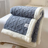 A thick gray fleece blanket with a white sherpa trim is folded on a white bed.