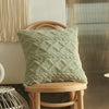 A textured sage green geometric plaid cushion cover resting on a light wooden stool.