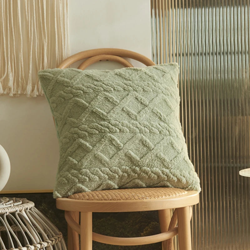 A textured sage green geometric plaid cushion cover resting on a light wooden stool.