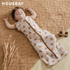 A baby is lying on a brown textured blanket wearing a beige soft cotton sleeping bag or swaddle.
