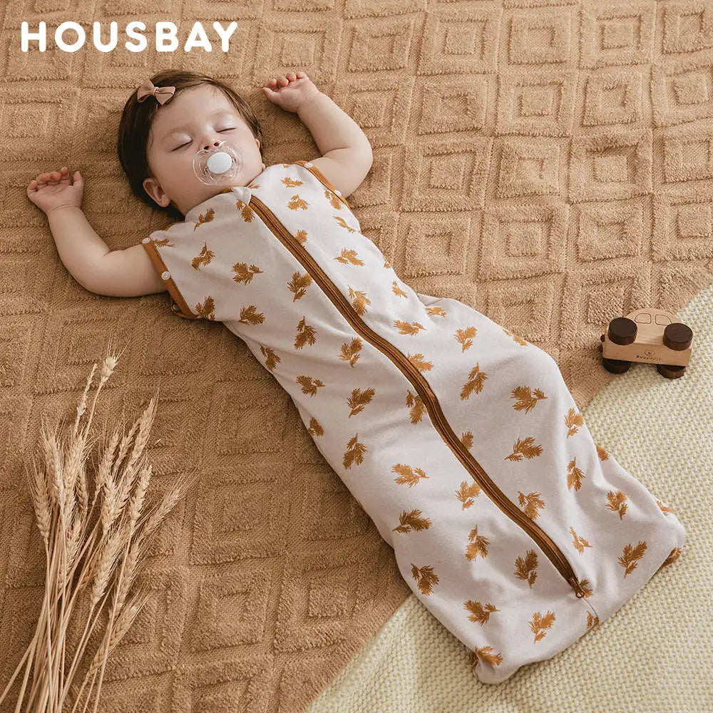 A baby is lying on a brown textured blanket wearing a beige soft cotton sleeping bag or swaddle.