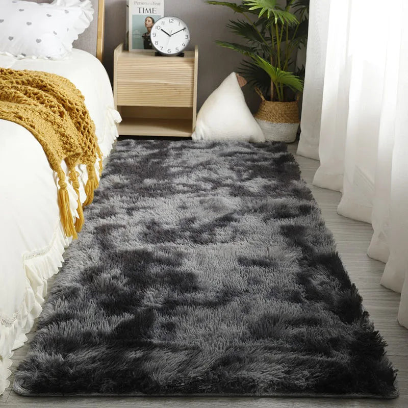 A dark gray faux fur rug placed on a wooden floor next to white bedding and potted greenery.