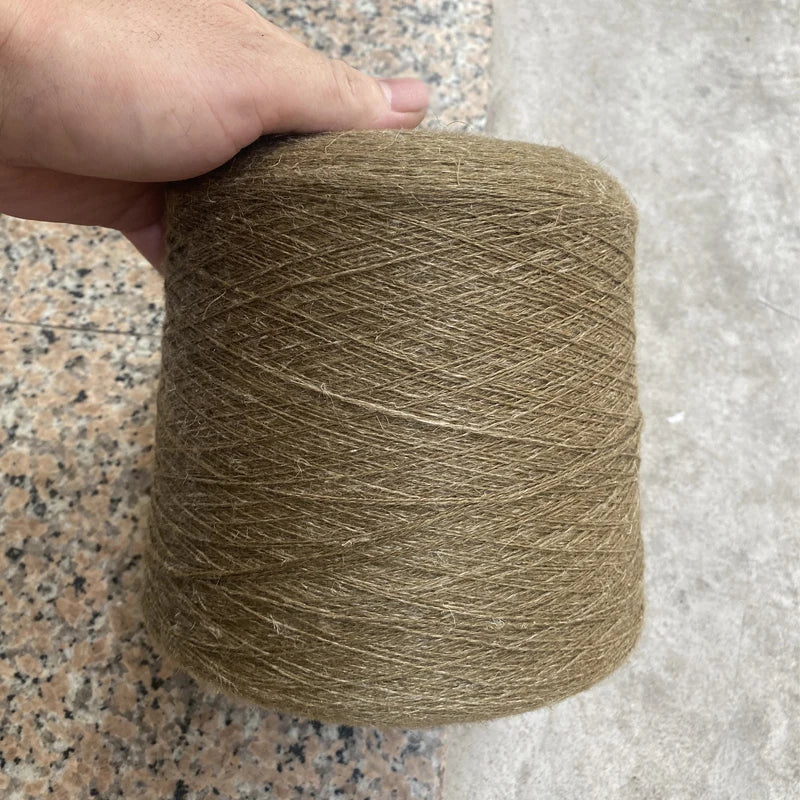 A hand is holding a large spool of natural beige hand-woven wool and linen blended yarn.