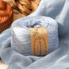 A ball of light blue yarn is draped over a knitted fabric, with a wooden basket in the background.
