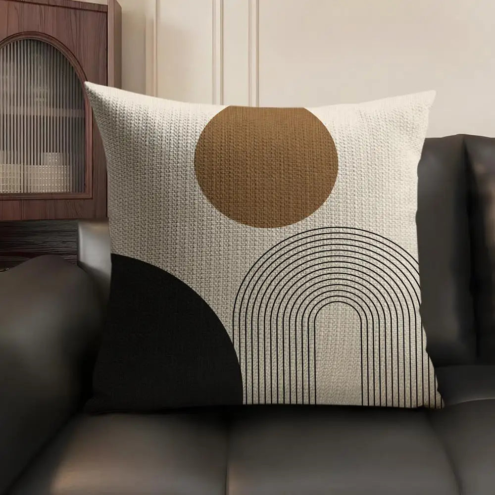 A beige cushion cover with a large circular brown design and black geometric lines on a dark leather sofa.