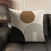 A beige cushion cover with a large circular brown design and black geometric lines on a dark sofa.