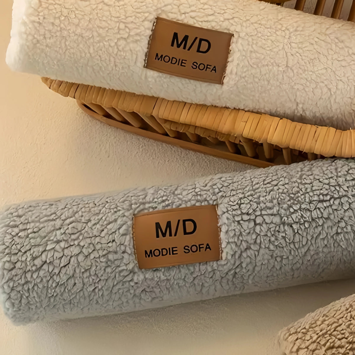 A white sherpa anti-slip sofa cover is placed on a woven tray next to a gray sherpa cover.