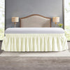 A cream colored wrap around elastic bed skirt with a white sheet and wooden headboard in a bedroom setting.