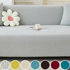 A light gray jacquard elastic sofa slipcover displayed on a sofa with matching pillows and decorative fabric swatches.