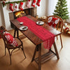 A wooden dining table decorated with a red lace table runner and festive Christmas decorations.