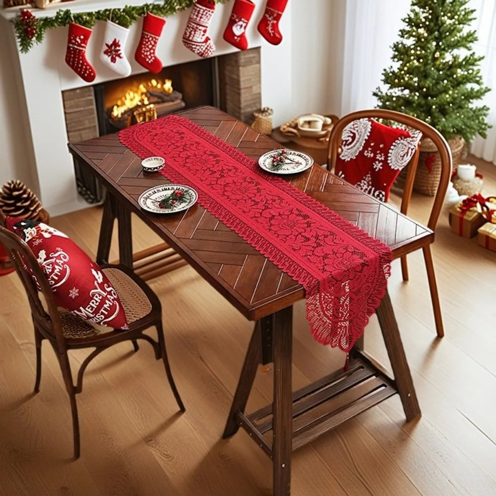 A wooden dining table decorated with a red lace table runner and festive Christmas decorations.