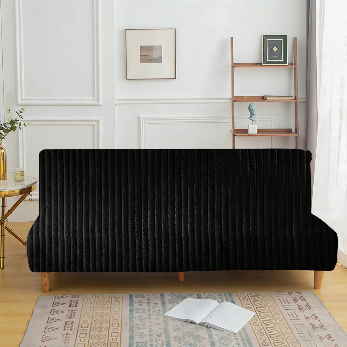 A black velvet armless sofa cover displayed on a wooden floor with an oriental rug.