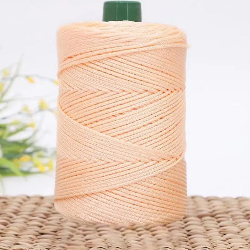 A spool of peach colored 3mm ice rope crochet yarn with a green cap, resting on a woven mat.