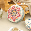 A round bohemian tatami cushion with intricate floral patterns rests on a wooden floor frame.