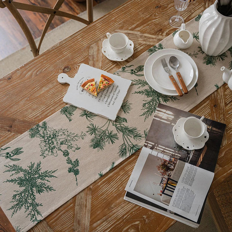 A checkered table runner with green foliage patterns is laid on a wooden table with white tableware.