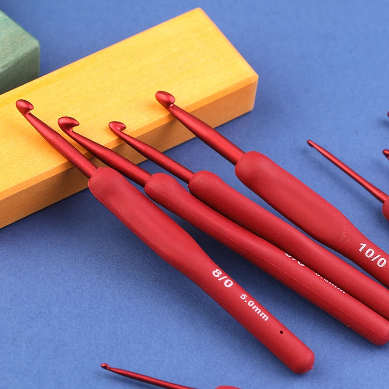 A set of red ergonomic crochet hooks resting on a yellow wooden block.