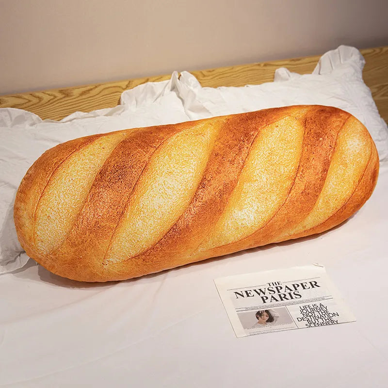A golden-brown baguette loaf resting on white fabric next to a newspaper.