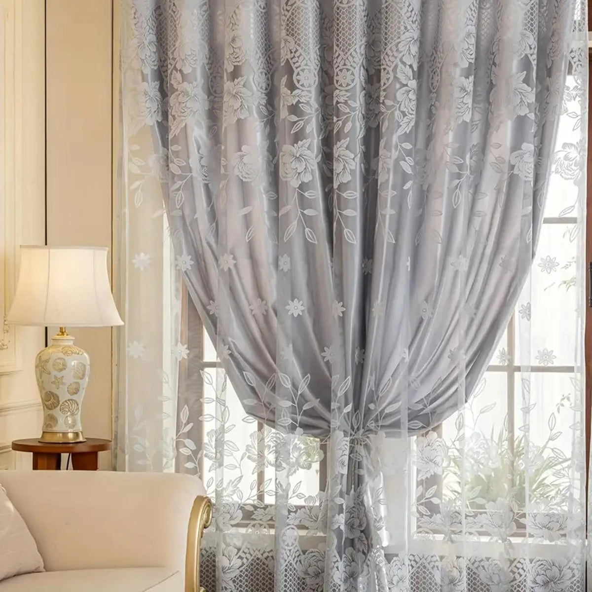 Gray vintage floral blackout curtain draped over a window with sheer lace overlay.