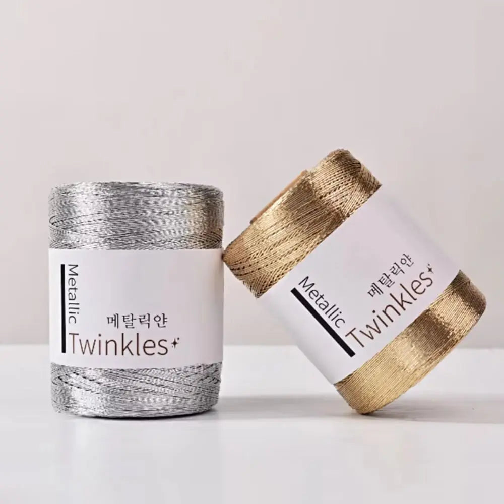A spool of metallic twinkles yarn in silver and gold is shown next to a rolled-up skein.