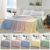 A display of various colored ice silk cooling blankets draped on a bed, showing shades of blue, gray, pink, yellow, and green