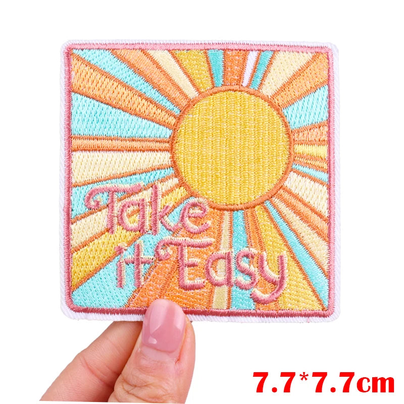 A square embroidered patch featuring a yellow sun with the text Take It Easy in pink thread.