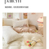 A close-up of a beige milk fleece blanket and duvet set with soft pillows and a pink lamp on a light-colored bed.