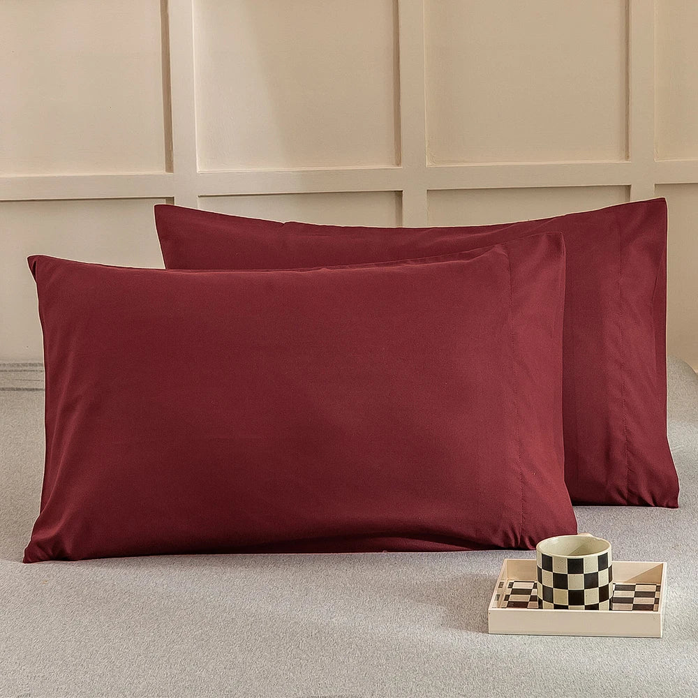 A deep maroon microfiber pillow cover is displayed on a light gray surface next to a small wooden box with checkered fabric s