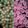 A close-up view of pink and green glow-in-the-dark glass seed beads in a bulk pack.