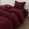 A deep burgundy duvet cover set with matching pillows and a folded blanket on a bed.