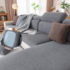 A gray plush elastic sofa cushion cover with neutral throw pillows and a patterned blanket on a modern sofa.