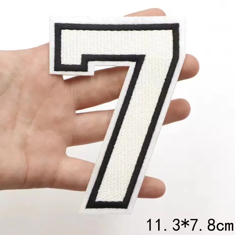 A hand holds a white and black embroidered number 7 letter patch for clothing decoration.
