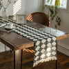 A black and white diamond patterned linen table runner on a rustic wooden dining table.