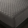 A close-up view of a dark gray waterproof quilted mattress protector on a bed.