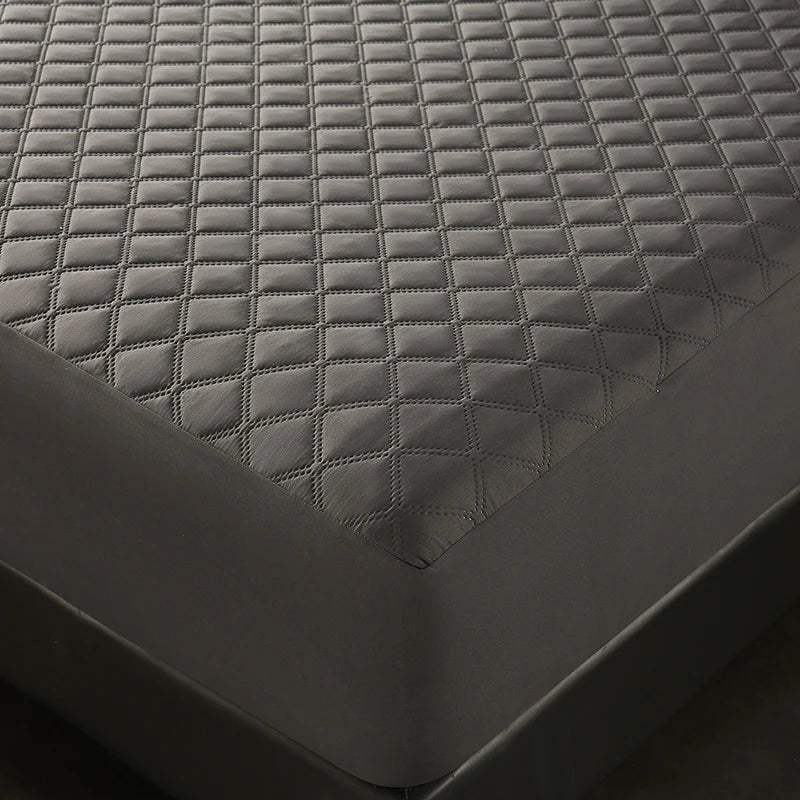 A close-up view of a dark gray waterproof quilted mattress protector on a bed.
