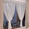 White floral lace sheer curtain panels hanging in a window with neutral drapery.