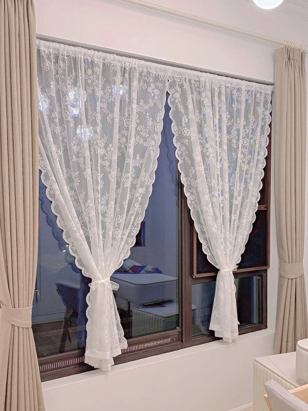 White floral lace sheer curtain panels hanging in a window with neutral drapery.