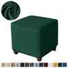 A dark emerald green velvet ottoman slipcover with a rolled fabric detail.